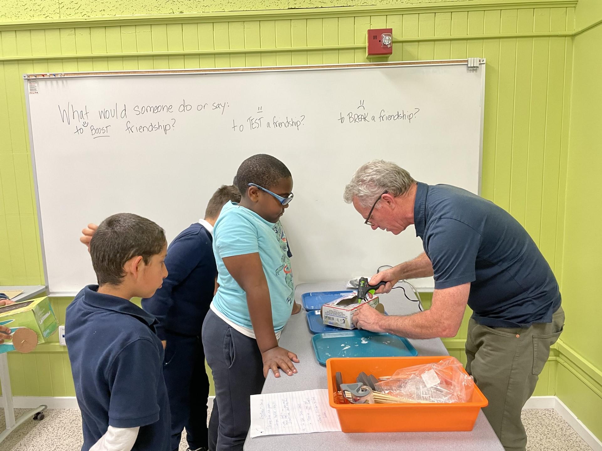Spruce Elementary fourth grade teacher Paul Summers helps students glue wheels onto their egg racer cars, which the students made out of shoe boxes. 